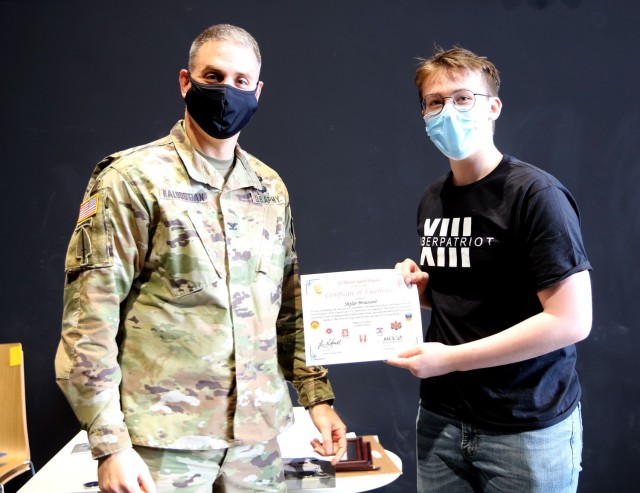 Col. Michael R. Kaloostian, 2nd Theater Signal Brigade Commander, presents Skylar Broussard with a Certificate of Excellence for his contributions to the Wiesbaden High School’s Air Force Association United States CyberPatriot program. Members...