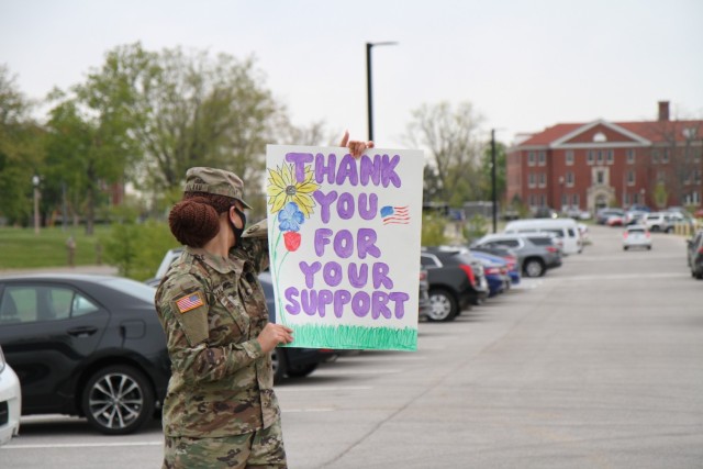 Sgt. Tuu Valaau, human resources noncommissioned officer, 1st Theater Sustainment Command, looks over her shoulder at children as they arrive at Kingsolver Elementary School, Fort Knox, Kentucky, April 23, 2021. The Soldiers created posters and...