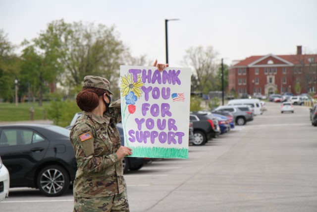 Sgt. Tuu Valaau, human resources noncommissioned officer, 1st Theater Sustainment Command, looks over her shoulder at children as they arrive at Kingsolver Elementary School, Fort Knox, Kentucky, April 23, 2021. The Soldiers created posters and cheered on the families of the Fort Knox community in observance of the Month of the Military Child. The month of April is designated as Month of the Military Child to let children know that their resiliency and ability to change and adapt is appreciated.  (U.S. Army photo by Staff Sgt. Nahjier Williams, 1st TSC PAO)