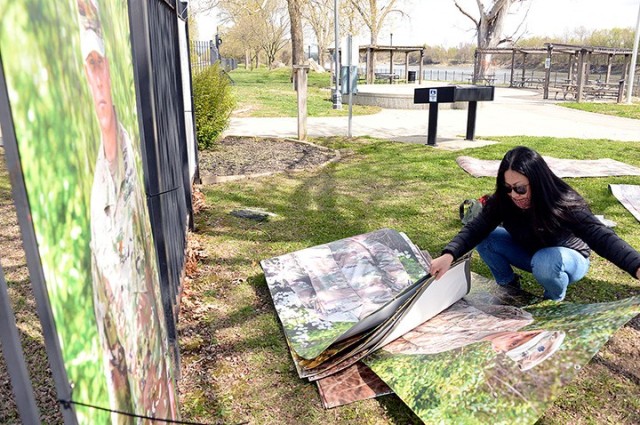 "To Be At War" community photography project facilitator Arin Yoon sorts through portraits of service members for the next one to affix to a fence, next to the portrait of Maj. Matt Lyles, while installing the open-air art exhibit April 21 at...