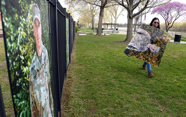 Arin Yoon, "To Be At War" community photography project facilitator, carries her portrait of Lt. Col. Matt Beall to add to a fence lined with of portraits of service members, including Maj. Brent Kinney, while installing the exhibit April 21 at...