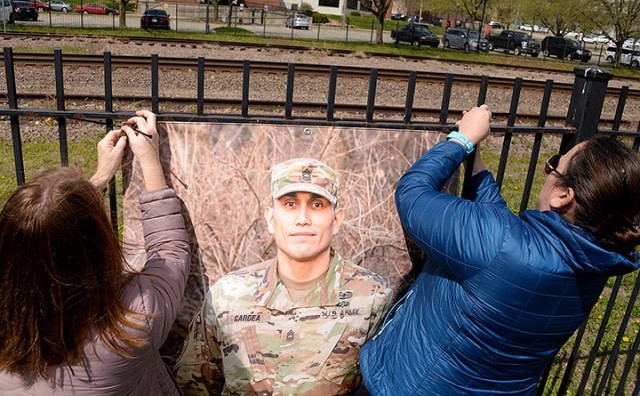"To Be At War" photography workshop participant Terri Lichlyter and volunteer Kerry Manneck hang a portrait of Master Sgt. Javier Gardea, taken by Arin Yoon, "To Be At War" community photography project facilitator, while helping install the...