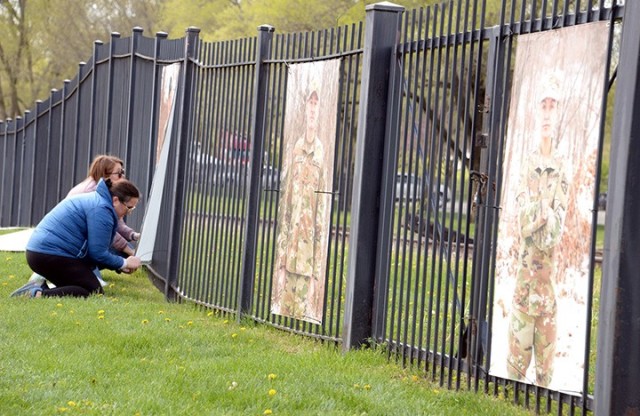 "To Be At War" photography workshop participant Terri Lichlyter and volunteer Kerry Manneck affix portraits of service members, taken by Arin Yoon, "To Be At War" community photography project facilitator, along a fence while helping install the...