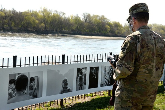 Lt. Col. Matt Beall, husband of "To Be At War" photography workshop participant Adrienne Beall, looks at his wife's photographs — including one of him shaving and another of their 1-year-old son Noble — featured in the "To Be At War" community...