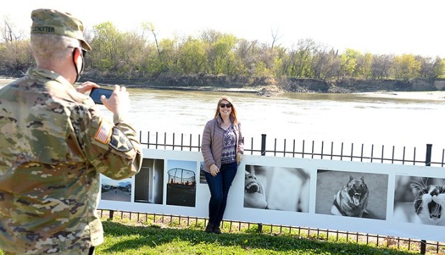 "To Be At War" photography workshop participant Terri Lichlyter poses for her husband, Maj. Dan Lichlyter, as he takes a photo of her with her photographs featured in the "To Be At War" community photography exhibit April 22 at Leavenworth Landing...