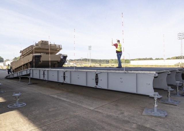 Barron Dulaney, a Defense Logistics Agency Distribution Anniston employee, is guided by Landon Magouryk, a DLA Distribution employee, as he drives an M1A1 Abrams tank onto a platform using a rear off-load platform configuration.