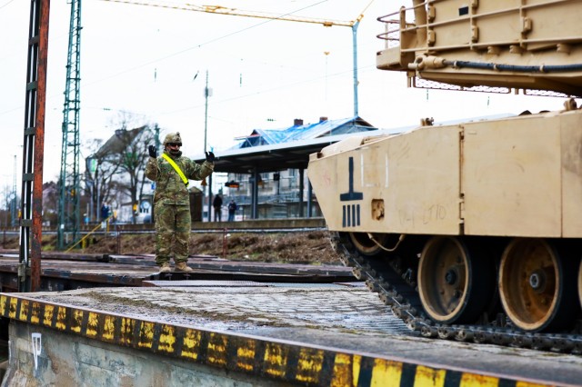 A U. S. Army Soldier assigned to the 1st Armored Brigade Combat Team, 1st Cavalry Division, guides an M1 Abrams Main Battle Tank onto a railcar in preparation for transfer to Poland, at Parsburg, Germany, Mar. 13, 2021