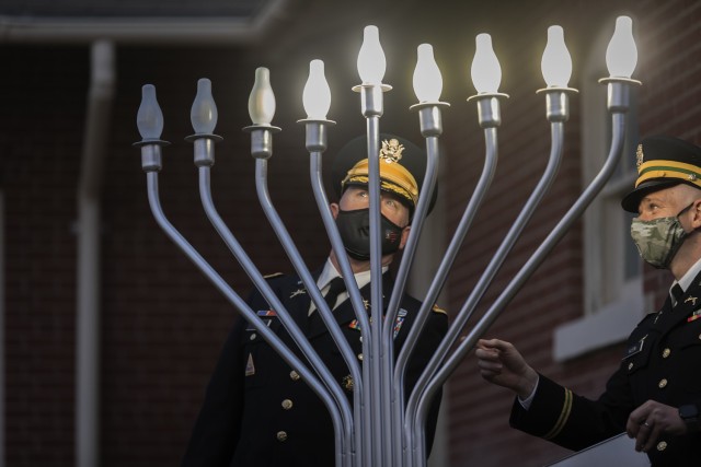 Colonel Stu James, the Fort Bliss garrison commander, lights the individual lights of the menorah outside of Chapel 3, while 1st Lt. Scott Klein (right), the Distinctive Religious Group Leader for the Jewish faith at Bliss, looks on at Fort Bliss, Texas, April 26, 2021. (U.S. Army photo by David Poe, USAG Fort Bliss)