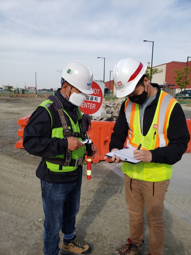 Dan Doan (right), an FED construction control representative, logs USAG Humphreys construction site visitors and conducts a mandatory temperature check on Kim Chong Ki (left), a site safety health officer, before repair on the Walk-in Gate parking...