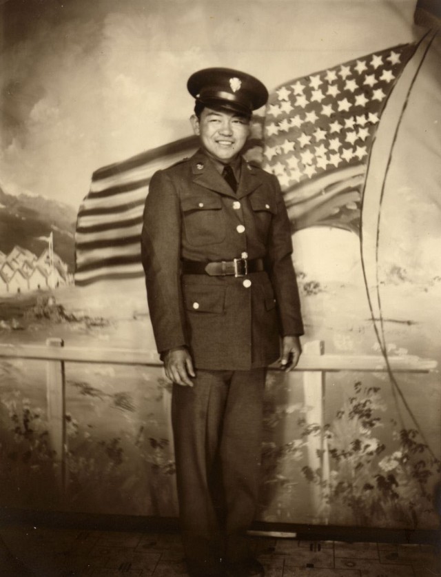 Army Pfc. Sadao Munemori smiles as he poses for a photo in front of a painting of a U.S. flag.