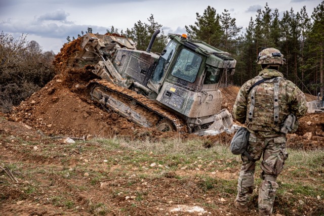 U.S. Army Pvt. Dalton Leonard, a D6K Light Bulldozer operator assigned to Beast Troop, Regimental Engineer Squadron, 2nd Cavalry Regiment, moves earth to create a berm and ditch to deter enemy movement in the area as part of exercise Dragoon Ready 21 at Hohenfels Training Area, Germany, April 17, 2021. Sgt. 1st Class Cody Williams, a platoon sergeant, also assigned to Beast Troop, ensures the earth modification standards are met. Dragoon Ready 21 is a 7th Army Training Command-led exercise, which provides the 2nd Cav. Regt. with the opportunity to en-hance readiness and train on its core tasks. (U.S. Army photo by Staff Sgt. Christopher Stewart)