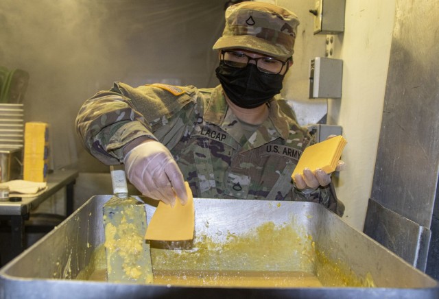 Pfc. Allaine Lacap from Fox Battery Forward Support Company, 2nd Regiment, 15th Field Artillery Battalion, 2nd Brigade Combat Team, 10th Mountain Division (LI) puts slices of cheese to mix with eggs for breakfast for Soldiers during a two-day field feeding operation and competition called the Philip A. Connelly Awards Program at Fort Drum, New York, May 6-7, 2021. Field feeding exercises are important for closing the nutrition gap Soldiers experience when they are out in the field. (U.S. Army photos by Spc. Pierre Osias)
