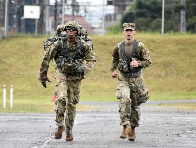 Sgt. Jamal Walker, assigned to the U.S. Army Japan Band, nears the finish line of the 12-mile ruck march during the 2021 U.S. Army Japan Best Warrior Competition at Sagami General Depot, Japan, May 13. Walker came in first in the ruck march with a time of 2 hours, 30 minutes, and also won the competition in the noncommissioned officer category. Staff Sgt. Christopher Williams runs with him.