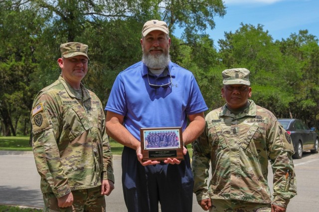 US Army Sgt. 1st Class Matthew Pennington, a counterintelligence agent (left), and Command Sgt. Maj. Michael R. Mabanag (right), both with the 504th Expeditionary Military Intelligence Brigade, presents Gary Wilder, Pennington’s former drill sergeant (center), with a gift in Lions Park, Temple, Texas on May 7, 2021. The gift is a picture of Pennington’s basic training class.
(US Army photo by Pfc. Anthony X. Sanchez, 7th Mobile Public Affairs Detachment)