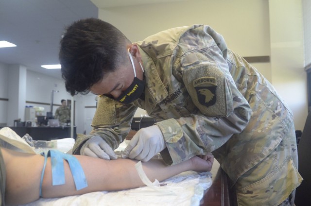 Specialist Ryan Do, Headquarters and Headquarters Battery, 101st Division Artillery, 101st Airborne Division (Air Assault) prepares an IV for Spc. Giovanny Rivera, Headquarters and Headquarters Battery, 101st Division Artillery, 101st Airborne...