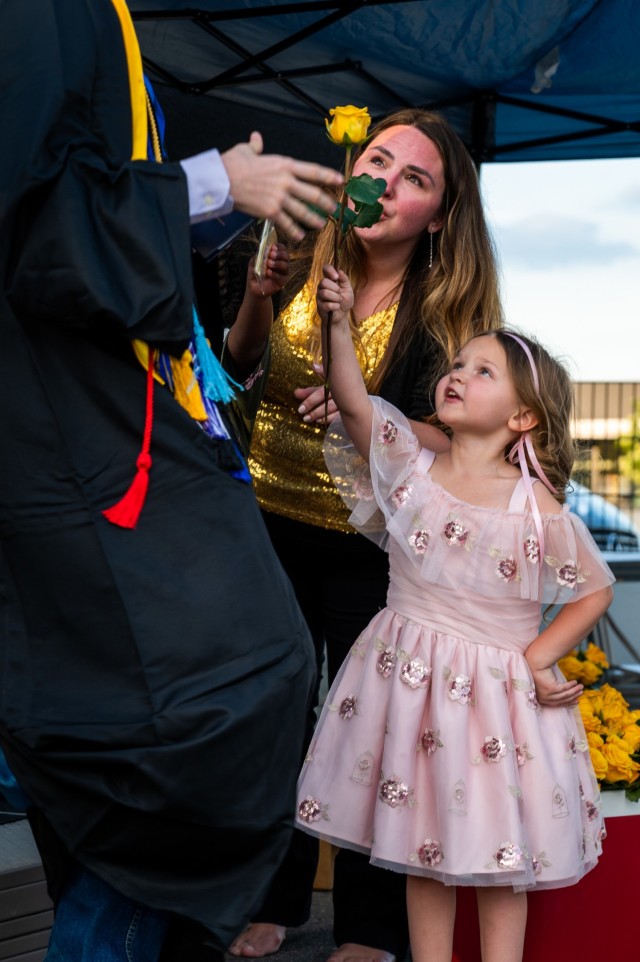 A girl gives a Stuttgart High School graduate a yellow rose as he walks off the graduation stage between an audience of cars during an outdoor, drive-in graduation ceremony at Panzer Barracks, Germany, June 2, 2021.