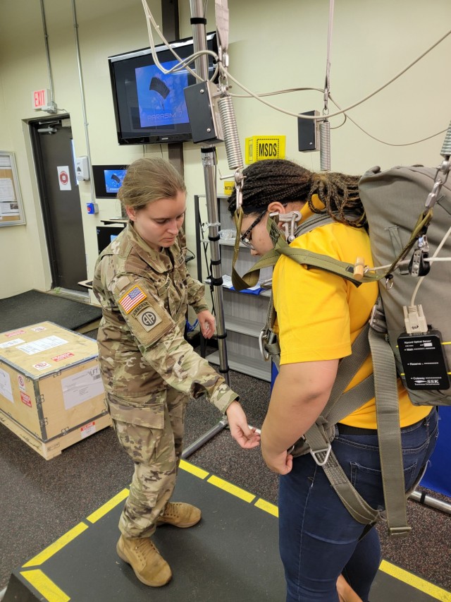 Spc. Alexia Smith, Airdrop Branch, prepares a cadet for static line jump simulation using the VR parachute simulator.
