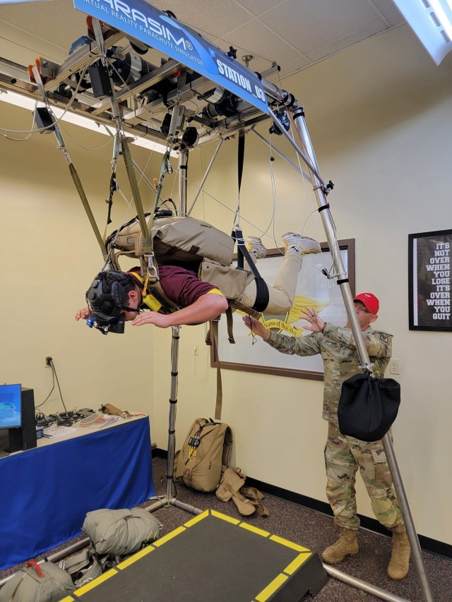 Warrant Officer Rhett Southard, Airdrop Branch, helps a cadet get in proper position for free fall on the virtual reality parachute simulator.
