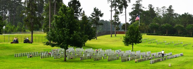Horticultural staff Junior Condon (left) and Marshall Evans mow the lawn at the Central Louisiana Veterans Cemetery as Vickey Stevenson removes old arrangements on the grave sites June 7.
