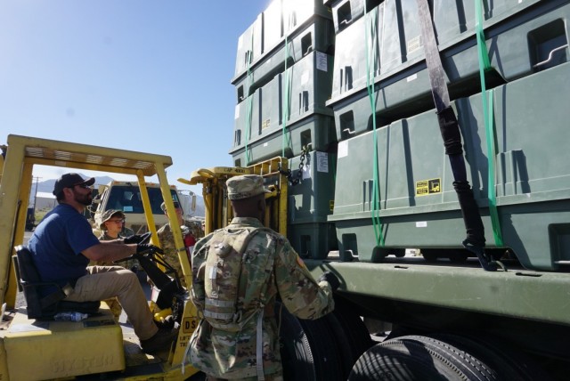 Forklift and operator place material on truck bed as soldiers strap down load