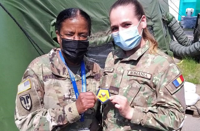U.S. Army Reserve Brig. Gen. Wanda N. Williams, commander of the 7th Mission Support Command, shares her coin and a photo with a Romanian Army Multi-National Command Southeast Soldier during a visit to MNC-SE headquarters for exercise DEFENDER-Europe 21 in Bucharest, Romania, June 13, 2021. Soldiers of the 209th Digital Liaison Detachment, 7th MSC, provided liaison capability between the U.S. Army´s V Corps, Joint Force Land Component Command and the Romanian MNC-SE.