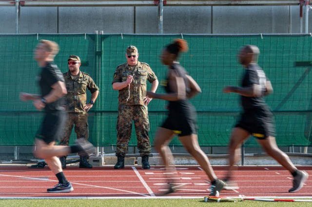 American Soldiers run past German Soldiers who are timing a 3-5 KM run during a German Sports Badge event on Panzer Kaserne, Germany, June 19, 2021.