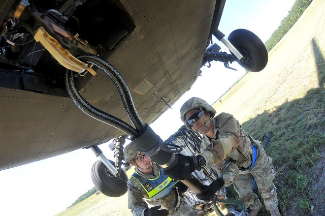 Pvt. NyKaya McLemore, with the help of her instructor, Staff Sgt. George Avery, uses the reach pendant to connect cargo to the underside of a 6-ton, hovering Black Hawk helicopter during sling load operations June 17 at McLaney Drop Zone.