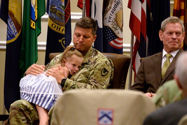 Incoming Garrison Commander Col. John Misenheimer Jr.'s daughter Juliana crawls into his lap during outgoing Garrison Commander Col. Harry Hung's remarks at the Garrison change of command, with ceremony host Vincent Grewatz, right, director of...