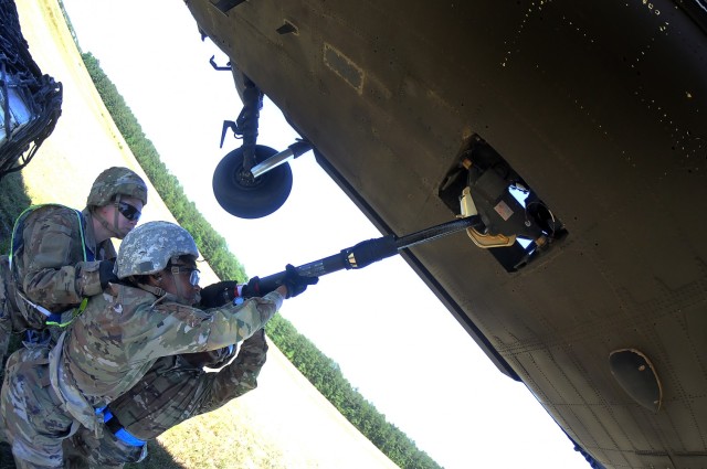 Pvt. Ibrahim Abukar and Pvt. Shekailah Davis – under the guidance of Staff Sgt. Jennifer Wynn  -- work together to hook the reach pendant to the underside of a UH-60 Black Hawk helicopter during a sling load operation June 17 at McLaney Drop Zone.