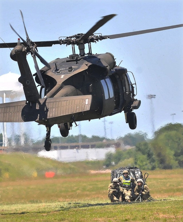 A UH-60 Black Hawk helicopter descends toward an instructor, ammunition specialist students and simulated cargo to perform a sling load operation June 17 at McLaney Drop Zone. The training event is part of the eight-week 89B Ammunition Specialist Course offered by the Ordnance School, an element of the U.S. Army Combined Arms Support Command.