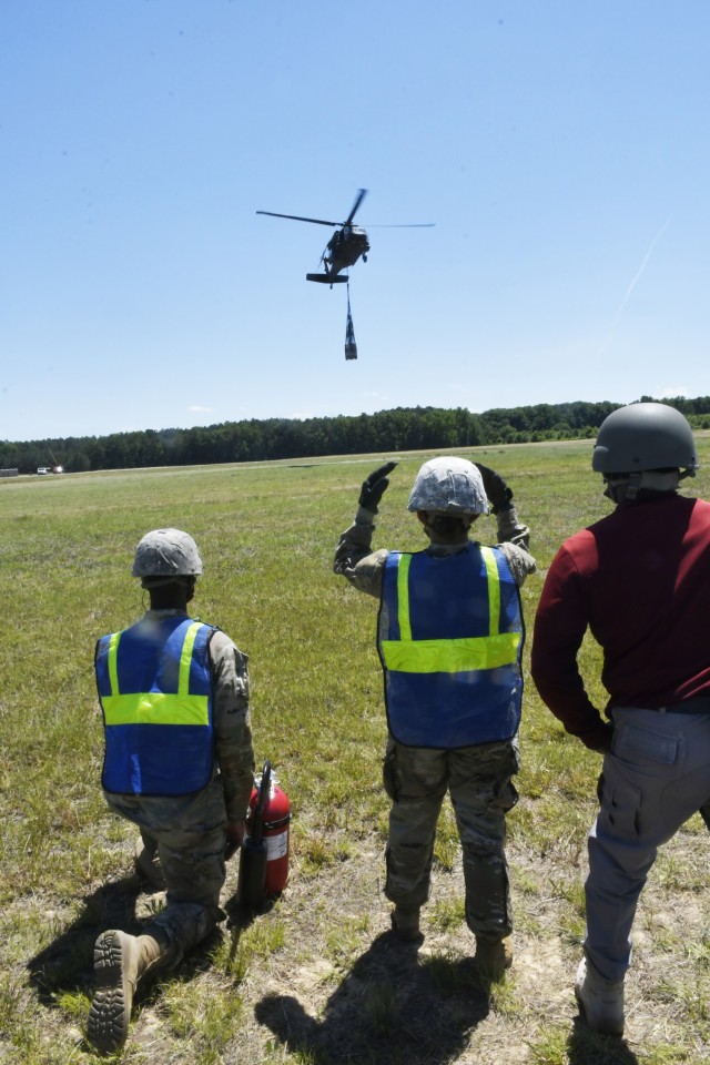 A student, under the guidance of an instructor, directs a UH-60 Black Hawk helicopter during sling load operations at McLaney Drop Zone June 17.