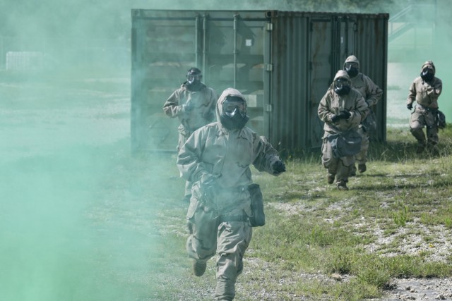 Test players wearing Level 4 MOPP gear advance to treat simulated casualties at Camp Bullis, TX.