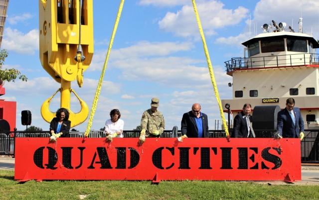 Rock Island District Commander, Col. Steve Sattinger and representatives from the five Quad Cities communities ceremoniously break champaign bottles on a sign suspended from the Rock Island District’s new heavy-lift crane, the Quad Cities.
