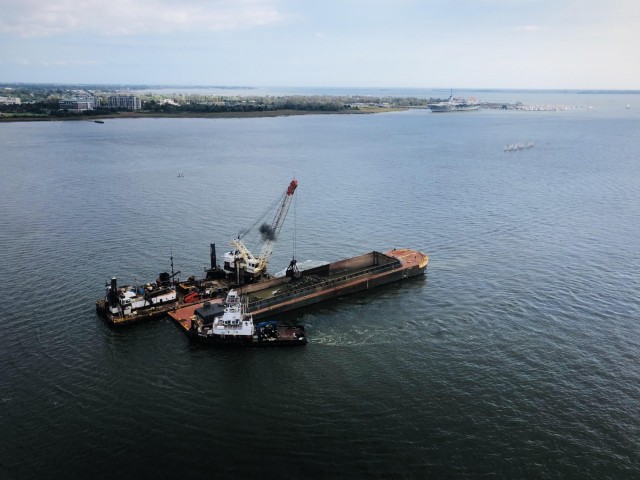 Vessel with crane moving dirt from ocean to basin.
