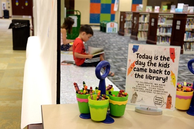Ten-year-old Brooklyn Lem and 6-year-old Colton Lem read their book selections in the children's room of the Combined Arms Research Library July 6. A large paper "canvas" has been hung just outside the children's room, with crayons and a drawing...