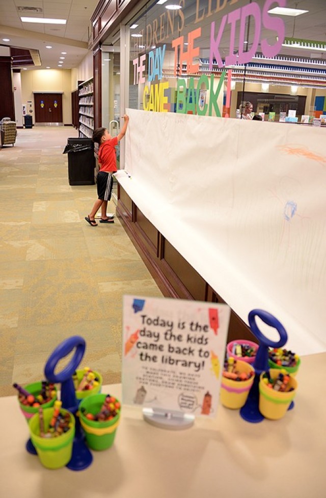 To help celebrate the reopening of the library, 6-year-old Colton Lem draws hearts, a deer and a tree on a paper "canvas" outside the children's room July 6 at the Combined Arms Research Library. Crayons and a drawing suggestion are positioned by...