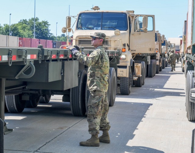 Row of trucks with soldier looing at trailer of first truck.