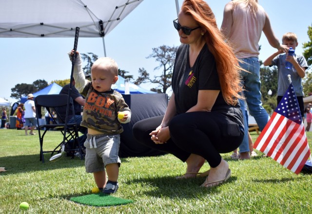 Chase Crook, 14 months, learns about golf during the “Party in the Park” at La Mesa Village, Monterey, Calif., July 9. His mother, Ashlee Crook, looks on.