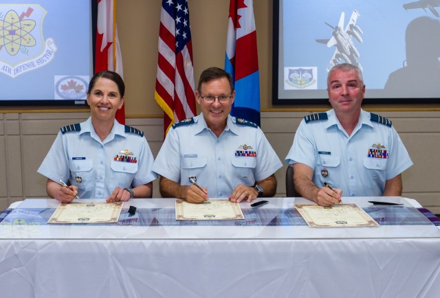 Royal Canadian Air Force Maj. Gen. Derek Joyce, center, Continental U.S. North American Aerospace Defense Region deputy commander, presides over the Canadian Detachment change of command July 8, 2021, at Joint Base Lewis-McChord, Washington. RCAF Lt. Col. Jody Hanson, left, assumes command from the outgoing commander, RCAF Lt. Col. Michael Fawcett, right, during the ceremonial signing of the change of command scrolls. (U.S. Air National Guard photo by Conrad Neumann)