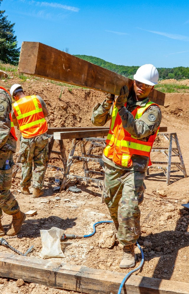 Sgt. Deivy Capellan, a horizontal engineer with third platoon, Argonaut Troop, Regimental Engineering Squadron, 2nd Cavalry Regiment, carries a piece of treated and stained lumber during the construction of a 100-meter trench on Hohenfels Training...