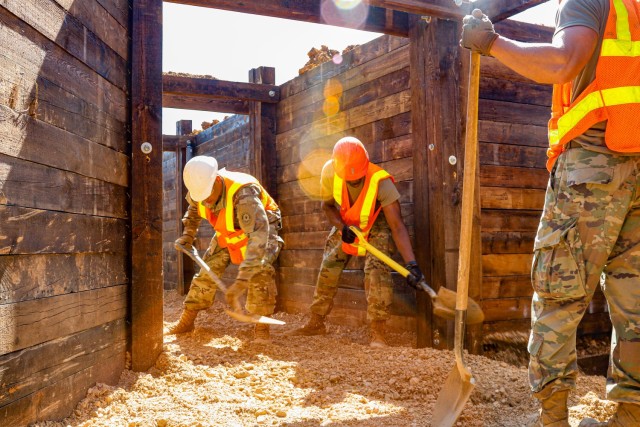 Sgt. Deivy Capellan, left, and Spc. Amade Ouedraogo, both horizontal construction engineers with third platoon, Argonaut Troop, Regimental Engineer Squadron, 2nd Cavalry Regiment, use shovels to level out a bucket full of gravel that had just been...