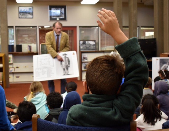 A child from the Porter Youth Center raises his hand as Cameron Binkley, command historian, Defense Language Institute Foreign Language Center, speaks to children at the Brig. Gen. Harry Dwight Chamberlin Library, Ord Military Community, Calif., July 15.
