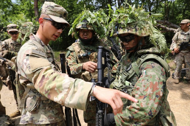 U.S. Army Spc. Vuongkhang Luong, an Adairsville, Georgia, native and infantryman with 1st Battalion, 28th Infantry Regiment "Black Lions," 3rd Infantry Division, points at the uniform of a Japan Ground Self-Defense Force member during exercise Orient Shield 21-2 at Aibano Training Area, Japan, June 24, 2021. Luong and other Black Lions trained alongside JGSDF members throughout the duration of the exercise.