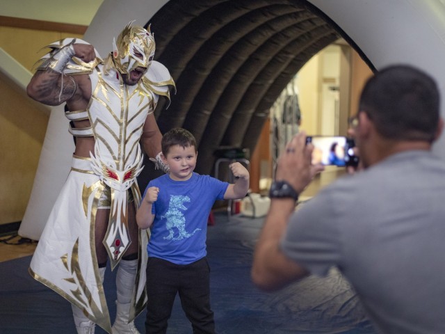 Army kid Jonah Orozco grabs a photo with a luchadore with help from dad, Sgt. Jaime Orozco, at the FMWR Lucha Libre wrestling event at Fort Bliss, Texas, July 23, 2021. “The best part was ‘the Dragon’ versus the chosen one,” said Jonah, “I had fun.”