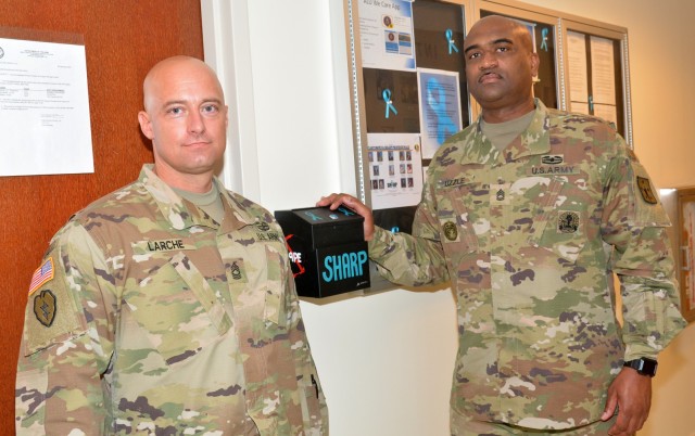 Sgt. 1st Class Towayne Uzzle and Master Sgt. John Larche – the incoming and outgoing sexual assault response coordinators, respectively, for the Army Logistics University – pose with one of the SHARP drop boxes that have been installed in each...