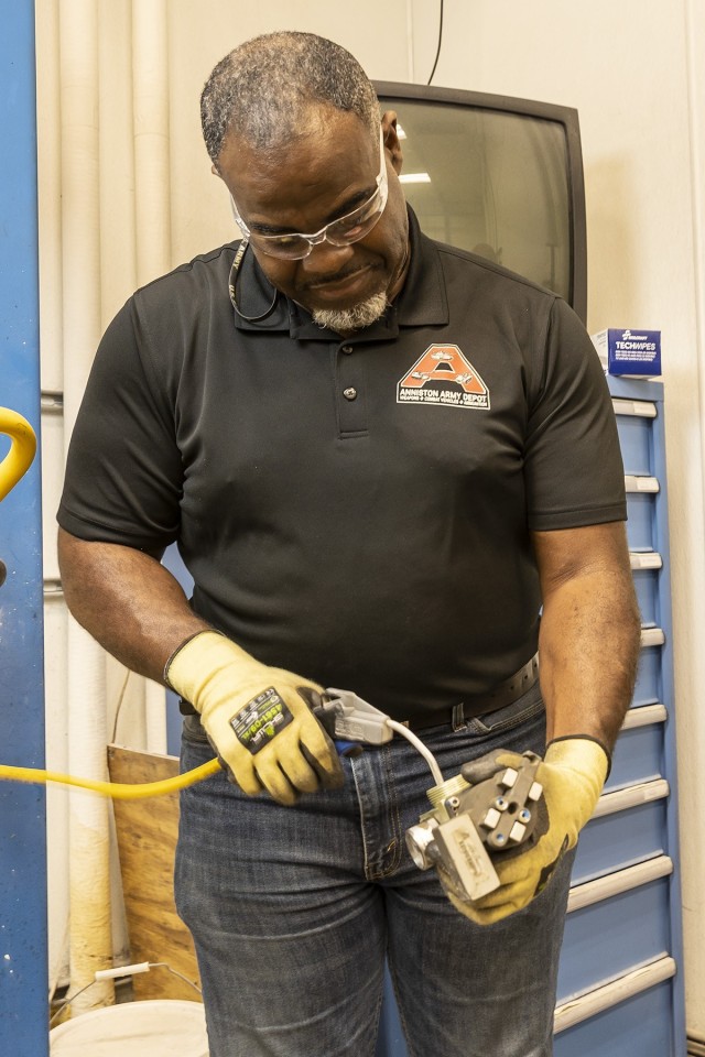 Destry White, and Anniston Army Depot artillery mechanic, uses an air hose to remove  dirt and debris from the valve of a fire bottle.