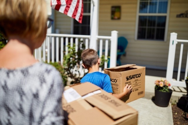 Stock photo of adult and child carrying moving boxes into a home
