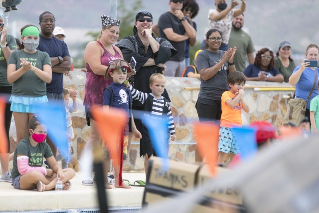 Clad in pirate gear,  Sgt. 1st Class Kyle Davis, his wife Danielle, and their family watch the races at the Cardboard Regatta at Fort Bliss, Texas, Aug. 14, 2021. Bliss Family and Morale, Welfare and Recreation held the annual event, which challenged contestants to build two-person vessels out of corrugated cardboard and tape and keep them afloat during racing at the Community Pool on west Bliss. “It’s about morale, keeping the morale up,” said Davis, a senior noncommissioned officer. “It’s a time to hang out with family.”