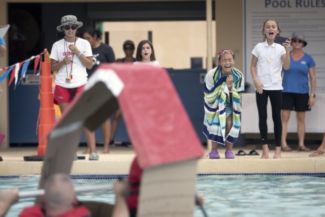 Well-wishers cheer a sinking team at the Cardboard Regatta at Fort Bliss, Texas, Aug. 14, 2021. Bliss Family and Morale, Welfare and Recreation held the annual event, which challenged contestants to build two-person vessels out of corrugated cardboard and tape and keep them afloat during racing at the Community Pool on west Bliss. “This really encompasses ‘family, morale, welfare and recreation,’  because, we know that for at least a month prior, for some of these people, they were working on their boats as a family,” said Michele Wiernicki, the Bliss FMWR marketing director and the day’s emcee.