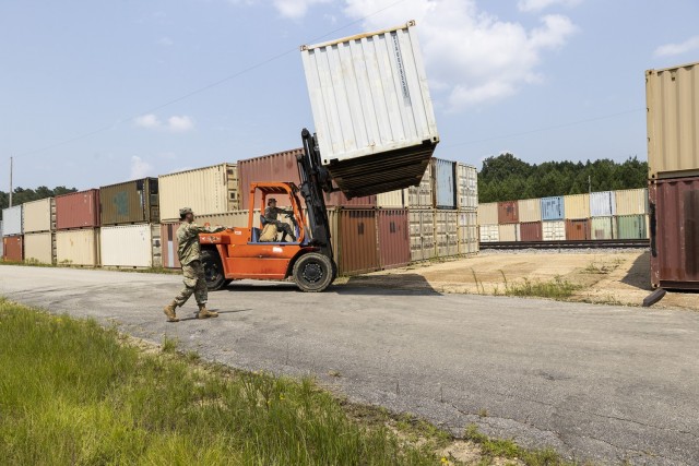 Spc. Veronica Rodriguez operates a heavy duty forklift by placing a container on wooden beams to help prevent moisture from causing rust on the bottom of the container.